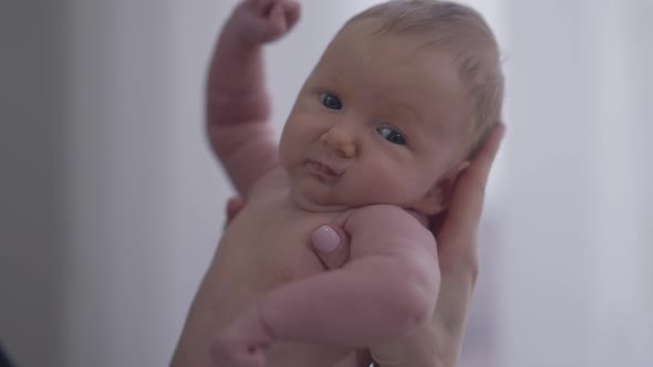 Small Naked Newborn Baby Girl in Female Hand Looking at Camera