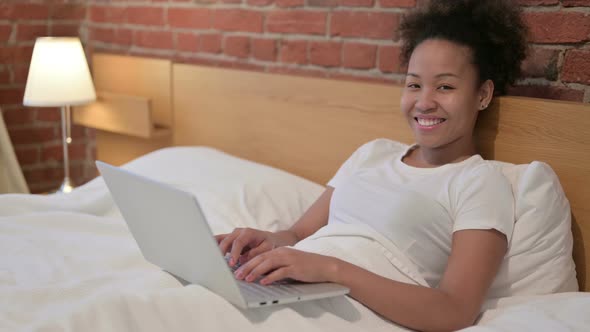 African Woman with Laptop Smiling at the Camera in Bed