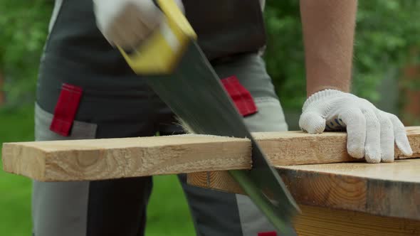Man Carpenter Saws a Wooden Board with a Hand Saw