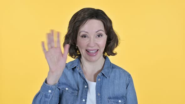 Old Woman Waving at the Camera in Yellow Background 