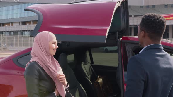 Muslim Female Dealer Showing Red Electric Car to African Male Customer Outdoors