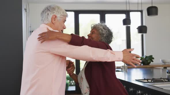 Happy senior diverse couple dancing in kitchen at retirement home