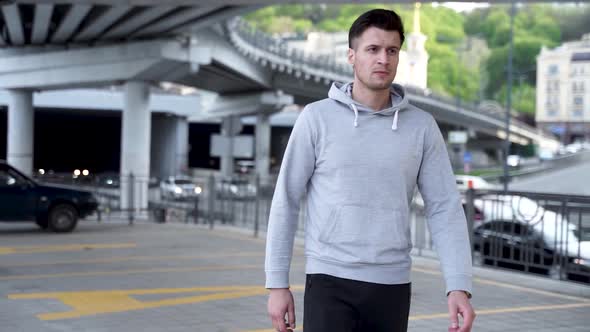 Close Up of Modern Sports Man Wearing Grey Jacket Walking Through Urban City