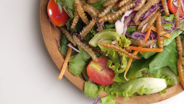 Vegetable salad with fried bamboo caterpillar in a wooden bowl.