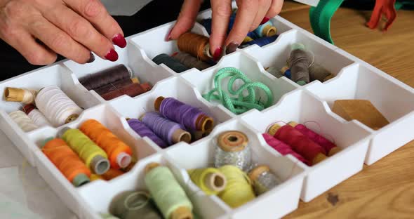 Step by step, woman's dressmaker hand pulls the thread out of the box