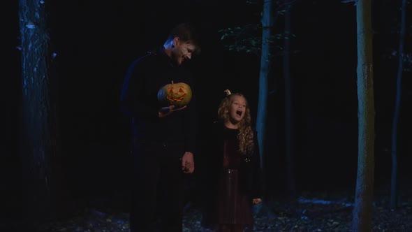 Portrait of Mysterious Vampire and Little Girl Holding Hands Standing in Dark Forest with