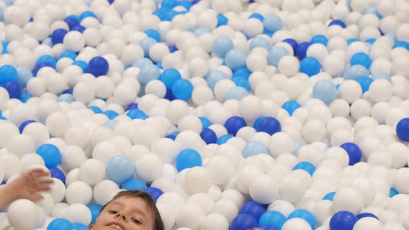 A cheerful Caucasian boy 6-7 years old in a children's play center bathes and burrows in colorful ba