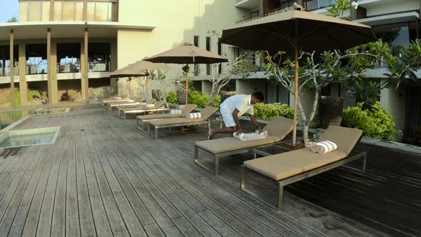 Pool Boy Arranging Folding Towels On Deck Chairs