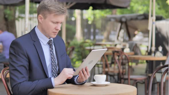 Businessman Celebrating Win on Tablet, Sitting in Outdoor Cafe