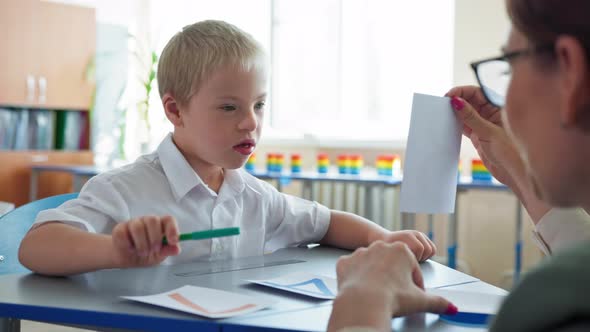 Life with Disabilities Boy with Downs Syndrome Studying Mathematics with Teacher Sitting at Desk in