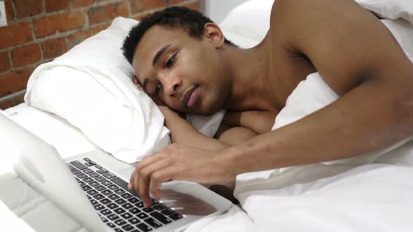 African Man Working on Laptop, Lying in Bed for Rest