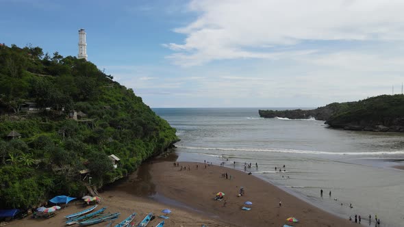 Aerial view of Baron Beach in Gunung Kidul, Indonesia with lighthouse and traditional boat.