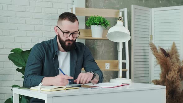 Bearded Man Learn Online Courses Using a Tablet and Write Notice in His Notebook