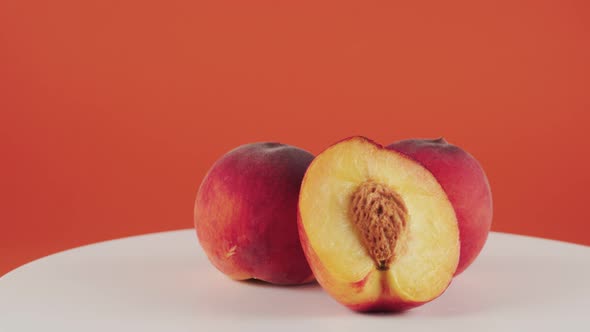 Close Up Half of Nectarine, Two Peaches on Rotating Table on Orange Background