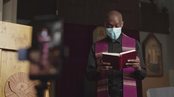 African-American Priest Wearing Mask Recording Sermon on Smartphone