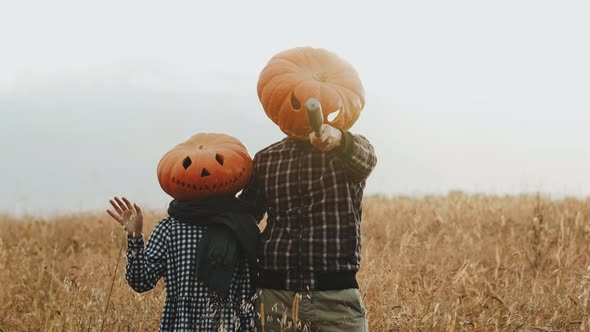 People with Large Pumpkins on Their Heads on Halloween Stand in a Field and Pose for a Camera