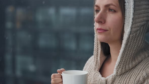 Woman Stays on Balcony During Snowfall with Cup of Hot Coffee or Tea