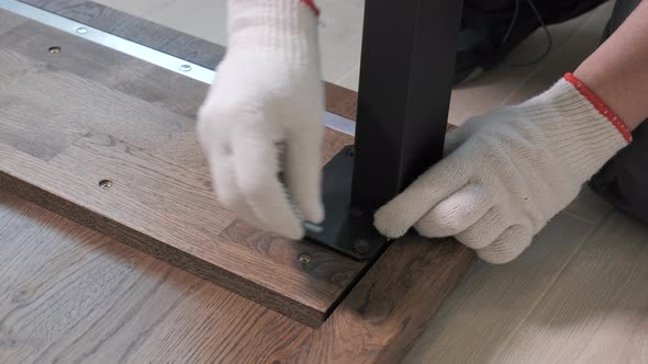 Builder in Overalls Screwing Table Legs Using a Screwdriver