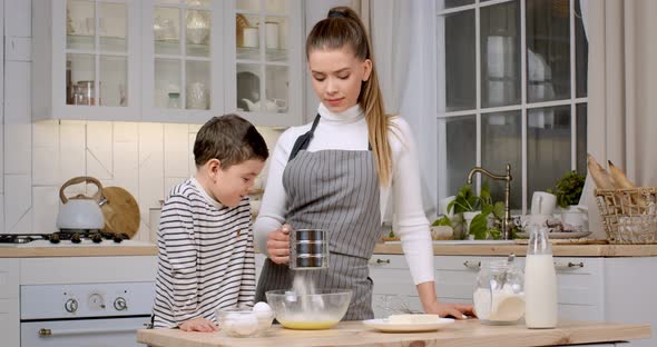 Young Mother in Apron Preparing Dough at Kitchen Her Curious Son Watching Process Slow Motion