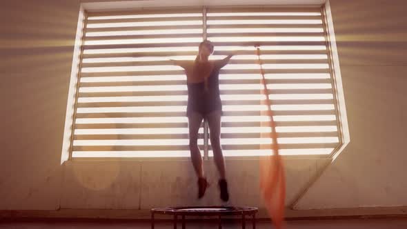 Bright volumetric light shines in the windows as a model demonstrats jumping on a fitness trampoline