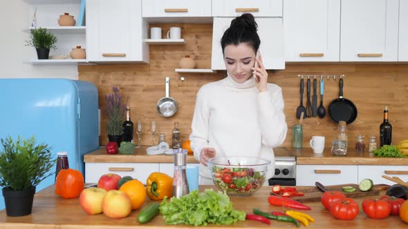 Young Female Talking On Cellphone While Cooking Healthy Food In Kitchen At Home.