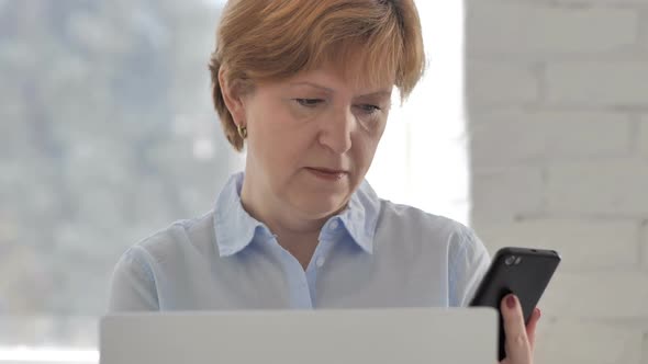 Old Woman Using Smartphone and Laptop for Work