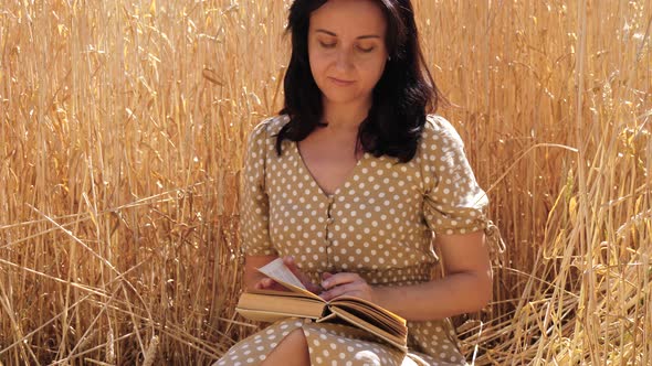 A Girl Reads a Book While Sitting in a Wheat Field and Enjoying the Nature of the Countryside