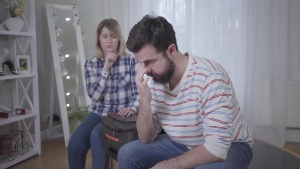 Depressed Caucasian Man Lowering Head and Holding It with Hands As Woman Sitting at the Background