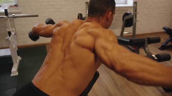 Bodybuilder in the Gym Does Dumbbell Raises While Lying on an Incline Bench Face Down to Work the