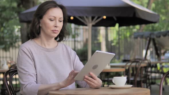 Online Video Chat on Tablet By Old Woman in Outdoor Cafe