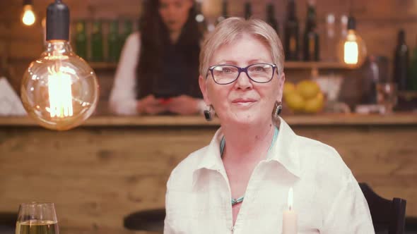 Portrait of a Beautiful Old Lady Sitting at a Table in a Bar