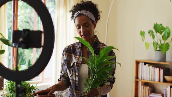 Mixed race female vlogger transplanting plants in pot and recording on smartphone at home