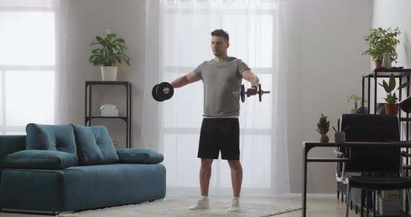 Sportsman Is Training with Dumbbells in Living Room Home Fitness and Healthy Lifestyle Tensing