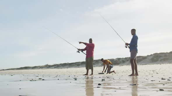 African american senior father and two teenage sons standing on a beach fishing and talking