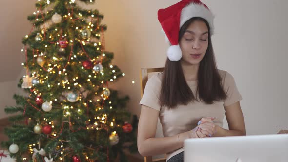 Young Brunette Female Student in Red Santa Hat Streaming Laptop Showing Gift Box