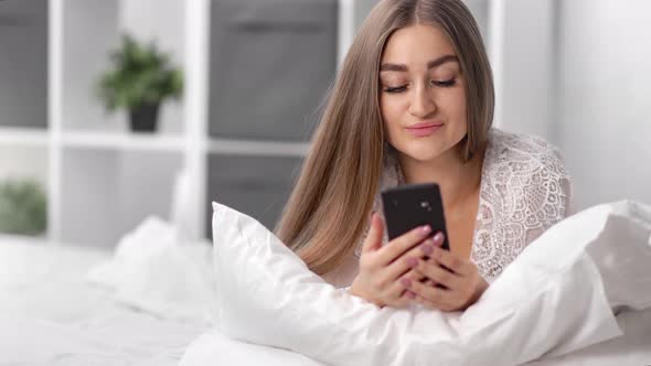 Portrait Beautiful Female in Pajamas Using Smartphone Lying on Bed