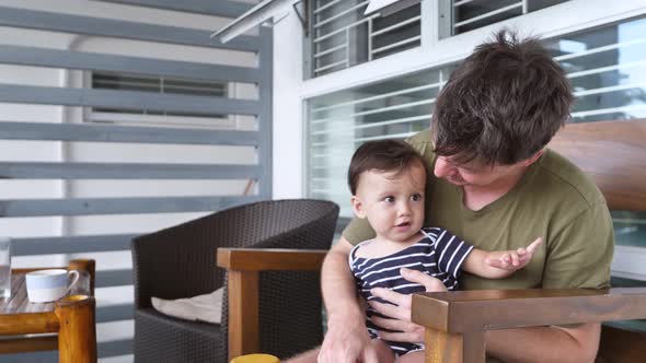 A Father Sits on a Chair with a Sweet Charming Son Less Than a Year Old and Watches His Child's