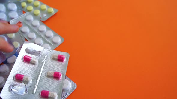 Close Up of Medical Blister Packs with Various Tablets on Orange Background. Man's Hand Selecting