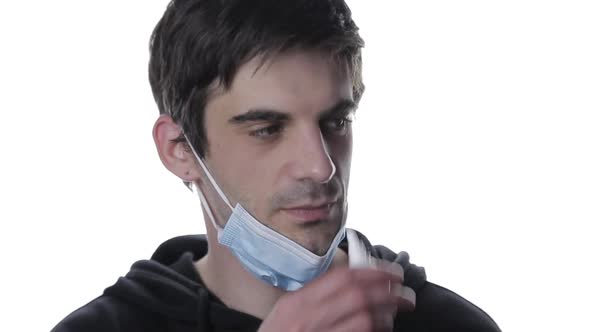 A Portrait of a Young Man Takes Off the Medical Mask and Sprays the Spray in the Nose in a White