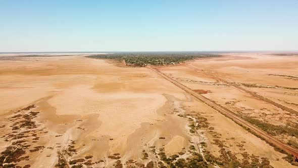 Long wide aerial shot of expansive barren wasteland surrounding bustling town in middle on no where.