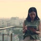 Beautiful woman using tablet chatting with friends while standing beside a balcony on a rooftop. - VideoHive Item for Sale