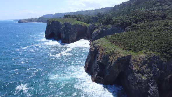 ocean waves crash into large coastal cliffs in Asturias Spain on bright sunny day