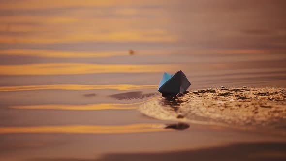 Origami boat on evening water background. Hand lets paper boat down into the water at sunset.