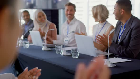 Audience and panel of business delegates applauding businessman at a conference