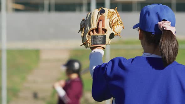 Diverse group of female baseball players in action on the field, returned ball caught by pitcher