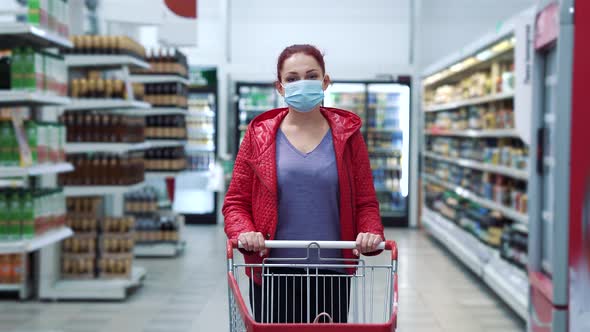 Woman in mask walking with shopping cart in mall