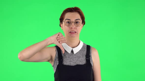 Portrait of Funny Girl in Round Glasses Is Showing Thumbs Down Gesture. Green Screen