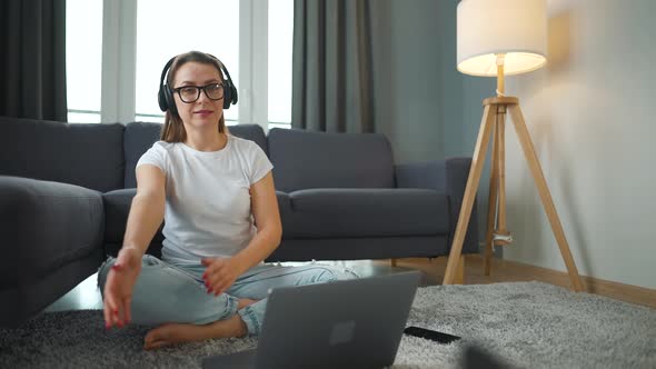 Casually Dressed Woman Sits on a Carpet with a Laptop in a Cozy Room and Lures a Fluffy Black Cat to