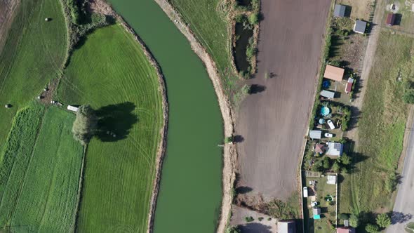 Aerial top down shot of a curvy river running among the fields, farms and gardens of a countryside f