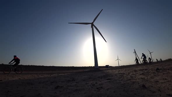 Cyclists Ride Along Road with a View of Windmills.